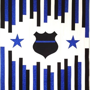 May include: A white background with blue and black vertical stripes. A black and blue police badge with a thin blue line is in the center. Two blue stars are on either side of the badge.