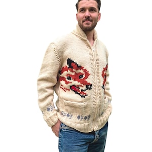 Può includere: Un cardigan con zip in maglia grossa color crema, caratterizzato da un grafico a testa di volpe rosso, nero e bianco sul davanti. Il maglione presenta un colletto a coste, maniche lunghe, due tasche frontali e un piccolo motivo floreale blu sull'orlo.