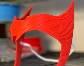 May include: A red plastic headband with a detailed design, resembling a crown or tiara. The headband is on a black metal shelf.