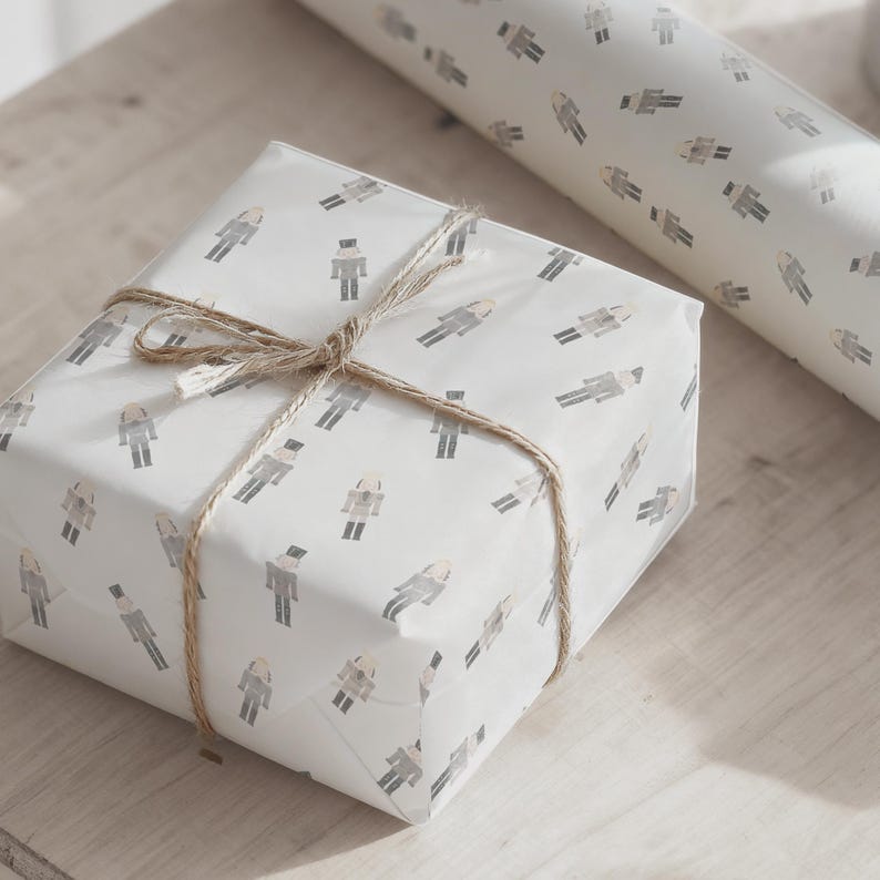 May include: A wrapped gift box and a roll of wrapping paper. The white paper is patterned with gray figures and tied with twine. The gift box is wrapped and tied with twine, and a small tag is attached.