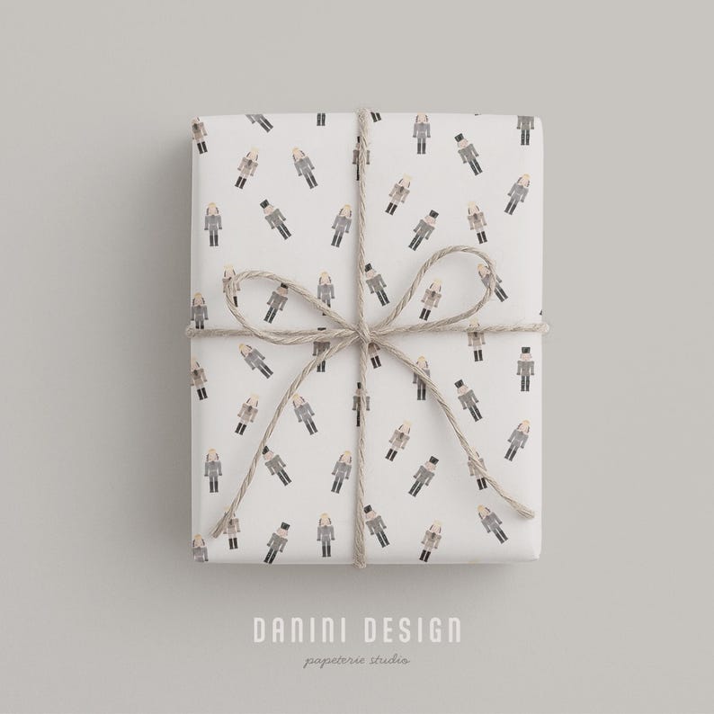 May include: A wrapped gift box with white paper featuring a repeating pattern of figures in coats and hats. The box is tied with twine in a bow. The text "DANINI DESIGN papeterie studio" is at the bottom.