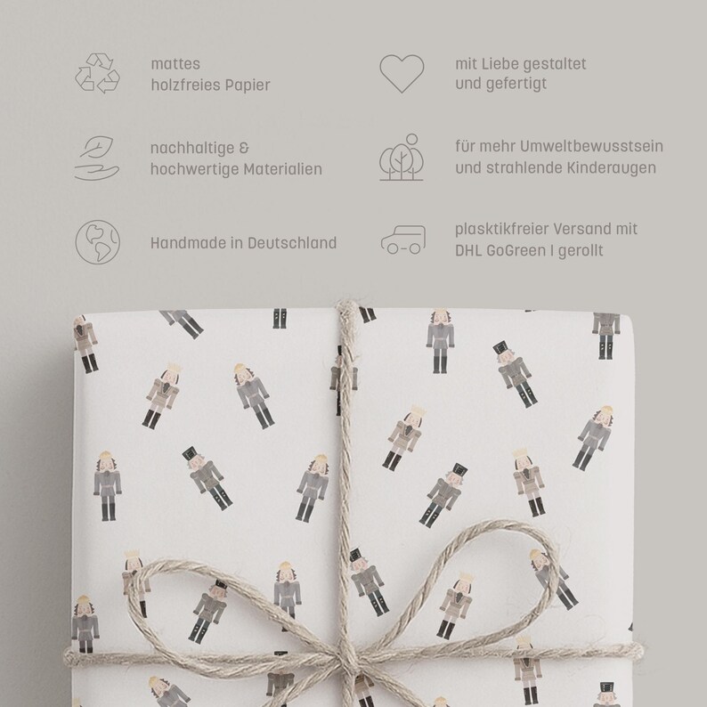 May include: White wrapping paper with a repeating pattern of nutcracker figures in gray, black, and tan. The paper is tied with twine. Text in German is visible in the background.