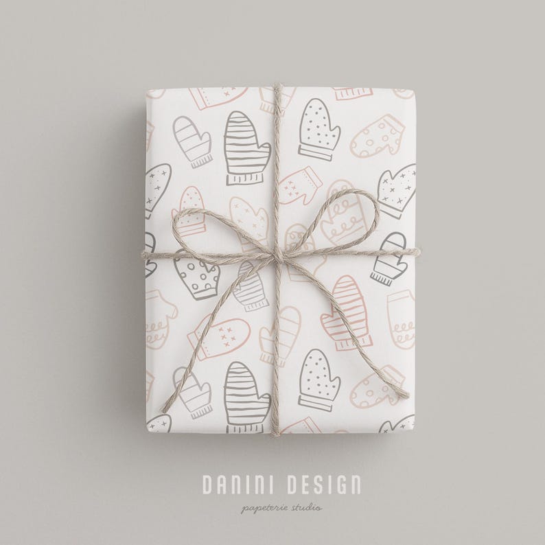 May include: A wrapped gift with a white background featuring a pattern of mittens in gray and pink. The gift is tied with twine and the text "DANINI DESIGN" and "papeterie studio" is printed on the bottom.