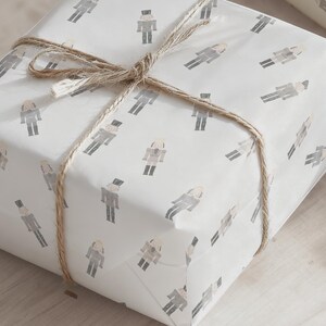 May include: A wrapped gift box featuring white paper with a repeating pattern of gray and beige nutcracker figures. The box is tied with natural twine, creating a rustic and festive presentation.