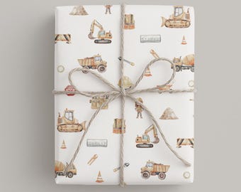 May include: A rectangular package wrapped in white paper featuring a repeating watercolor pattern of yellow construction vehicles, orange traffic cones, safety vests, tools, and piles of dirt, tied with a natural brown twine bow.