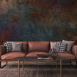 May include: A brown leather sofa with three cushions and two throw pillows. The sofa is in front of a wall with a textured, rusty, and blue paint finish. A coffee table with a dark wood top and gold metal legs sits in front of the sofa.