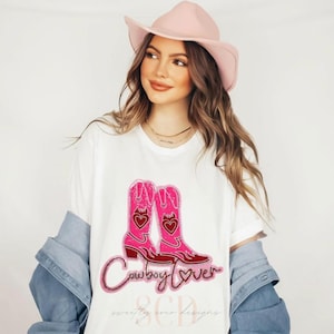 Op de afbeelding: Een wit T-shirt met een roze en rood glitterontwerp van cowboylaarzen en de tekst "Cowboy Lover".