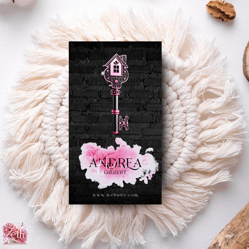 May include: Black and white business card with a pink watercolor design. The design features a key with a house-shaped head. The text on the card reads "Andrea Gilbert" and "www.website.com".