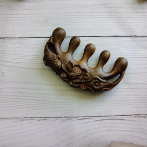 May include: A dark brown wooden hair comb with five prongs and intricate carvings of a fish and flowers.