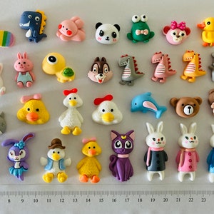 May include: A collection of 25 colourful, cartoon-style animal and character figurines. The figurines are made of a soft, pliable material and are approximately 2.5 cm in size. The figurines include a variety of animals, such as a panda, a frog, a duck, a rabbit, a chicken, a dolphin, a bear, and a cat. There are also some cartoon characters, such as a dinosaur, a turtle, and a squirrel.