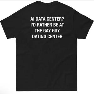 May include: A black short-sleeved t-shirt featuring white text printed on the back that reads: AI DATA CENTER? I’D RATHER BE AT THE GAY GUY DATING CENTER. The garment has a standard crew neckline and a plain, solid black fabric construction.