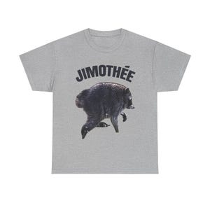May include: A heather gray short-sleeve t-shirt featuring a black graphic of a bear in motion. Above the bear, the text JIMOTHÉE is printed in a bold, dark, sans-serif font. The shirt has a crew neckline and a standard, straight-cut silhouette.