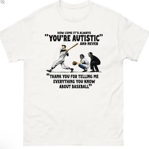 May include: A white short-sleeved t-shirt featuring a graphic of a baseball game with a batter, catcher, and umpire. The text reads: HOW COME IT'S ALWAYS "YOU'RE AUTISTIC" AND NEVER "THANK YOU FOR TELLING ME EVERYTHING YOU KNOW ABOUT BASEBALL".