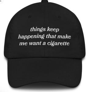 May include: Black baseball cap with white embroidered text that reads "things keep happening that make me want a cigarette". The cap has a curved brim and a rounded crown.