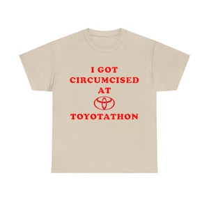May include: Beige t-shirt with red text that reads "I GOT CIRCUMCISED AT TOYOTATHON" with the Toyota logo. The shirt is a crew neck style.