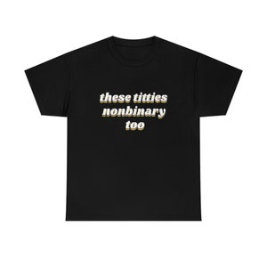 May include: Black t-shirt featuring the text "these titties nonbinary too" in a retro font with a yellow outline. The t-shirt has a crew neck.