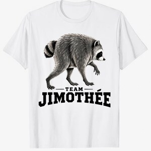 May include: A white short-sleeved t-shirt featuring a detailed black and white illustration of a raccoon walking. Below the raccoon, the text reads "TEAM" in small letters and "JIMOTHÉE" in large, bold, black capital letters centered on the chest.