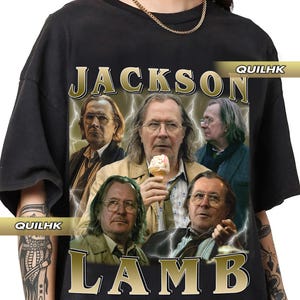 Puede incluir: Camiseta negra con un gráfico dorado de Jackson Lamb, un personaje de la serie de televisión "The Night Manager." El gráfico presenta cuatro hombres, uno sosteniendo un cono de helado, y el texto "Jackson Lamb" en letras doradas.