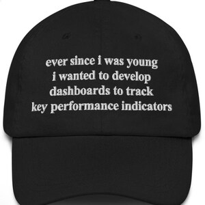 Op de afbeelding: Zwarte baseballcap met witte geborduurde tekst: "sinds ik jong was wilde ik dashboards ontwikkelen om key performance indicators te volgen."