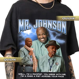 May include: Black t-shirt featuring a graphic print of three men wearing green shirts. The text "MR. JOHNSON" is printed in blue and white. The text "WELL, I'M A PACIFIST. YOU MESS WITH ME, I'M-A PASS A FIST ACROSS YOUR FACE" is printed in white.