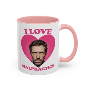 Puede incluir: Taza de cerámica blanca con interior y asa rosas. La taza presenta el texto "I LOVE MALPRACTICE" en rosa, con un corazón rosa que contiene un retrato de un hombre.