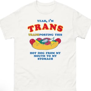 Puede incluir: Camiseta blanca con un gráfico de perrito caliente y texto: "Yeah, I'm TRANS transporting this hot dog from my mouth to my stomach."