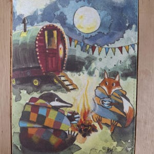 May include: A watercolour illustration depicting a caravan, a full moon, and a campfire. A fox and a mole, wrapped in blankets, are enjoying drinks. The scene is set against a night sky with colourful bunting, creating a whimsical atmosphere.