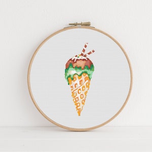 May include: A cross-stitch pattern of an ice cream cone with green and brown ice cream, topped with a red and white candy stick.