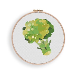 Puede incluir: Un patrón de punto de cruz de brócoli verde y amarillo en un aro de bordado de madera.