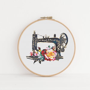May include: A vintage-style sewing machine cross-stitch embroidery hoop with a floral design. The sewing machine is black and gold with a floral design. The flowers are red, yellow, and pink.