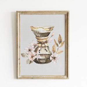 May include: A framed watercolor painting of a coffee maker with a floral design. The coffee maker is brown and has a white filter. The flowers are pink and white and are arranged around the coffee maker.