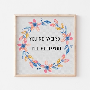 May include: A framed cross-stitch design with a floral wreath and the text "You're weird I'll keep you".