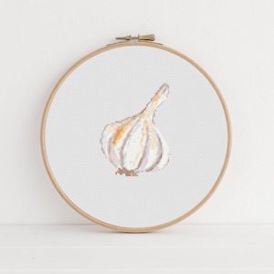 May include: A white garlic clove with a brown stem, embroidered on a white canvas in a wooden embroidery hoop.