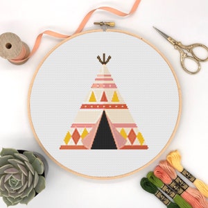 May include: A cross-stitch pattern of a colorful teepee tent with geometric designs in shades of pink, orange, yellow, and white. The teepee is framed in a wooden embroidery hoop.