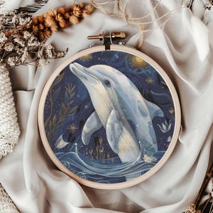May include: A framed embroidery hoop featuring a watercolor painting of a dolphin leaping from the ocean. The artwork is set against a dark blue background with stars and aquatic plants. The dolphin is light blue and white.