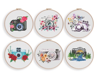 May include: Six embroidery hoop designs featuring vintage cameras with floral and nature-inspired accents. The cameras are decorated with watercolor flowers, leaves, and a mountain scene.