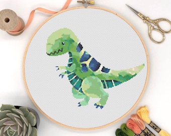 May include: A green and blue dinosaur cross stitch pattern in a wooden embroidery hoop. The pattern is on white Aida cloth and includes floss in green, blue, and yellow.