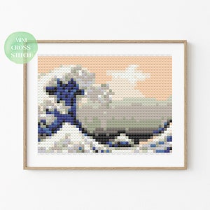 May include: A cross stitch pattern of a famous Japanese wave painting. The wave is blue and white with a light orange background. The pattern is in a wooden frame.
