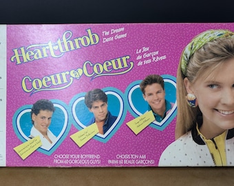 Puede incluir: Una caja de juego de mesa vintage con el título "Heartthrob Coeur Coeur" en rosa y azul. La caja presenta imágenes de hombres jóvenes y una mujer. El texto en la caja incluye "¡Elige a tu novio entre 60 chicos guapos!"