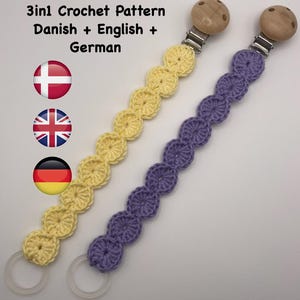 May include: Two crochet pacifier clips. One is yellow, the other is purple. Each clip has a wooden bead and metal clip at one end and a clear plastic ring at the other. The image includes text that reads "3in1 Crochet Pattern Danish + English + German".