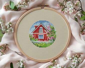 May include: A cross-stitch embroidery hoop featuring a red house with a white picket fence, surrounded by pink and green foliage. The design is set against a light beige fabric, framed by a wooden hoop. The background is a soft, pink fabric.