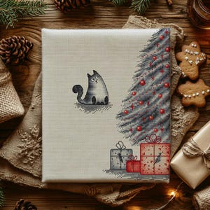 May include: A square cross-stitch embroidery on light beige fabric featuring a grey cat looking up at a stylised Christmas tree decorated with red ornaments. Below the tree are three wrapped gift boxes in red and grey with simple line details.