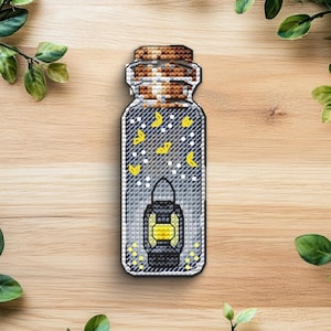 Può includere: Un oggetto decorativo a forma di barattolo con un design a lanterna. Il barattolo è riempito di farfalle gialle e punti bianchi, con un coperchio marrone e beige. La lanterna è nera e gialla. L'oggetto è posto su uno sfondo di legno.