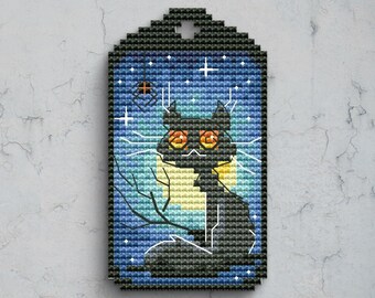 May include: A rectangular cross-stitch tag featuring a black cat with orange eyes sitting against a yellow full moon. The background is a blue night sky with white stars and a small spider hanging from a web. The border is a dark black frame.