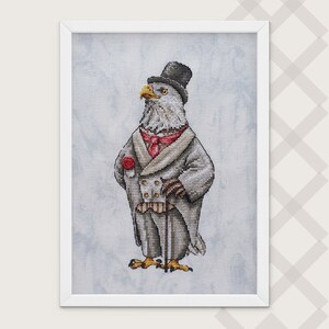May include: A framed cross-stitch embroidery depicting a bald eagle dressed in a formal gray tailcoat, a black top hat, a red cravat, and a red rose boutonniere. The eagle holds a thin walking cane and stands against a light blue mottled fabric.