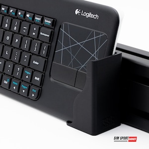 Puede incluir: Teclado inal&aacute;mbrico Logitech negro con panel t&aacute;ctil integrado. El teclado tiene un dise&ntilde;o QWERTY completo con teclas de funci&oacute;n y teclado num&eacute;rico. El panel t&aacute;ctil presenta un dise&ntilde;o geom&eacute;trico. El teclado se muestra en un soporte negro.