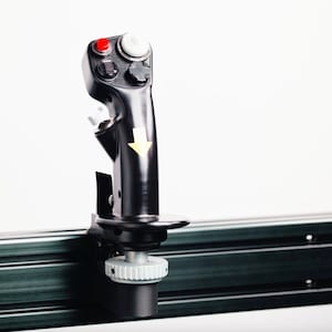 Könnte beinhalten: Ein schwarzer Joystick mit einem roten Knopf und einem weißen Knopf. Der Joystick ist an einer schwarzen Metallschiene befestigt.