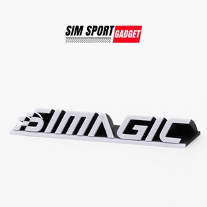 Puede incluir: Logotipo blanco impreso en 3D con el texto "SIMMAGIC" en letras negras. El logotipo está sobre un fondo blanco.
