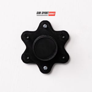 May include: A black, six-pointed star-shaped object with a circular indentation in the center. The object has five small screws around the perimeter.