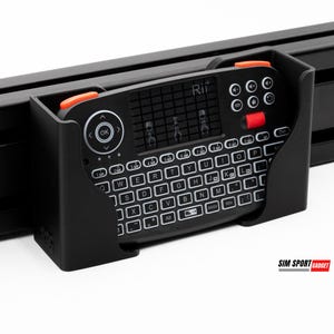 Puede incluir: Un mini teclado negro con teclas blancas y detalles en naranja est&aacute; montado en un marco negro. El teclado tiene un panel t&aacute;ctil y botones de funci&oacute;n. La marca "Rii" es visible.